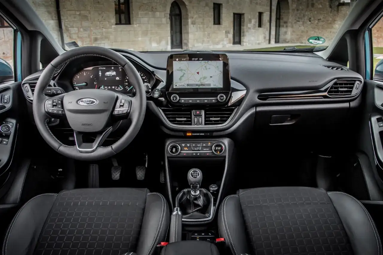 Wnętrze Ford Fiesta MK9: kierownica, ekran nawigacji, dźwignia zmiany biegów i czarne fotele.
