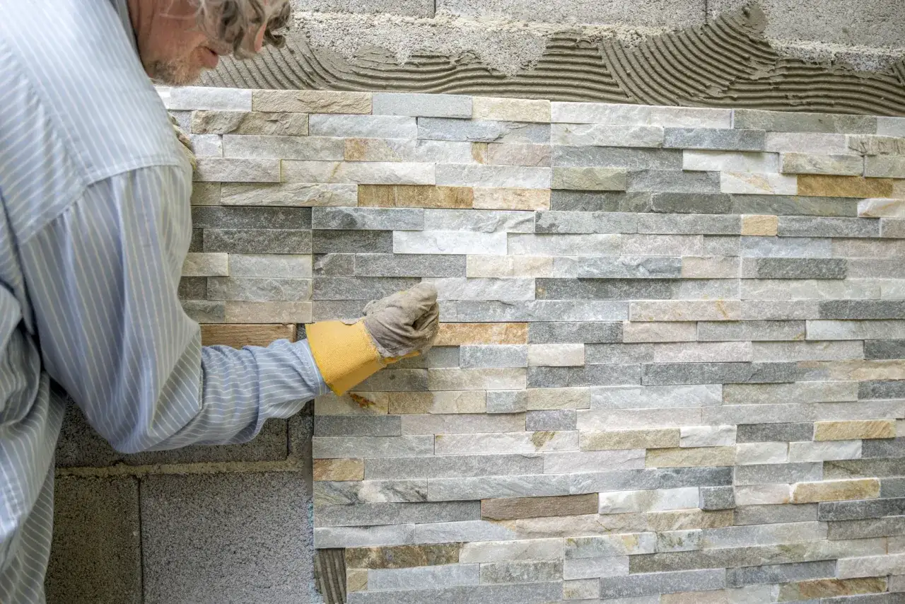 Un artisan pose des pierres de parement en quinconce sur un mur. La pose est minutieuse, cr&eacute;ant un motif naturel et textur&eacute;.