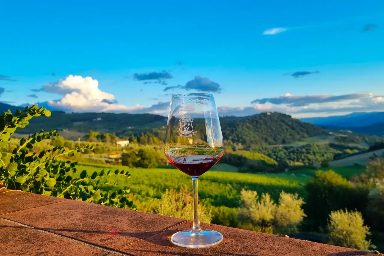 Calice di vino rosso con vista sui vigneti toscani al tramonto. Un assaggio delle cantine Firenze.