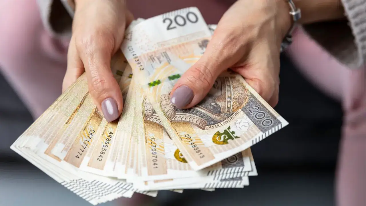 Dłonie trzymają stos banknotów 200 zł. Czy to pieniądze na podatek od spadków i darowizn?
