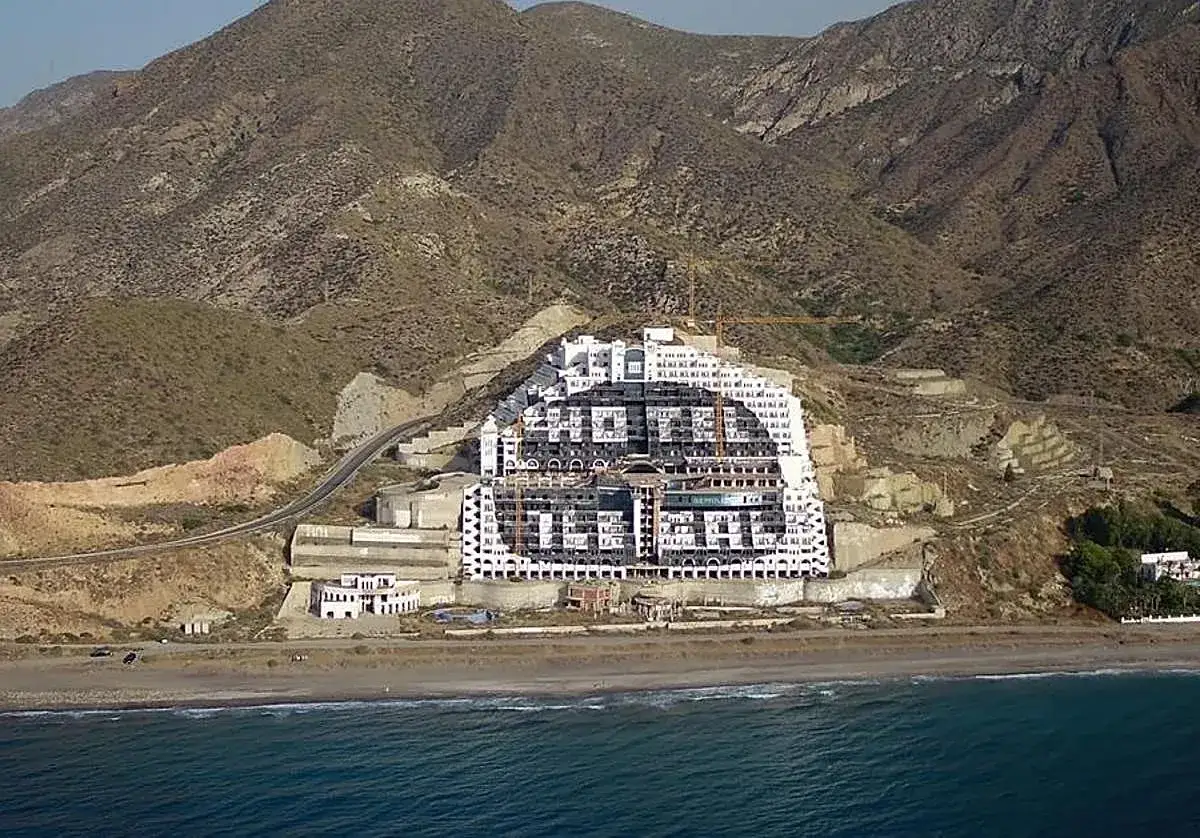 Edificio inacabado en la playa del Algarrobico, con montañas áridas al fondo y el mar en primer plano.