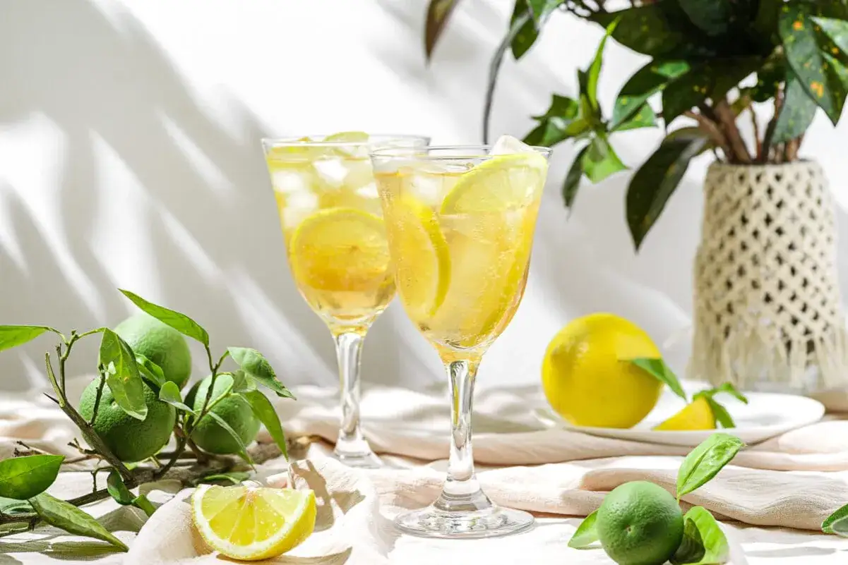 Dwa orzeźwiające drinki z limoncello, ozdobione plasterkami cytryny i lodem, na tle świeżych owoców cytrusowych.