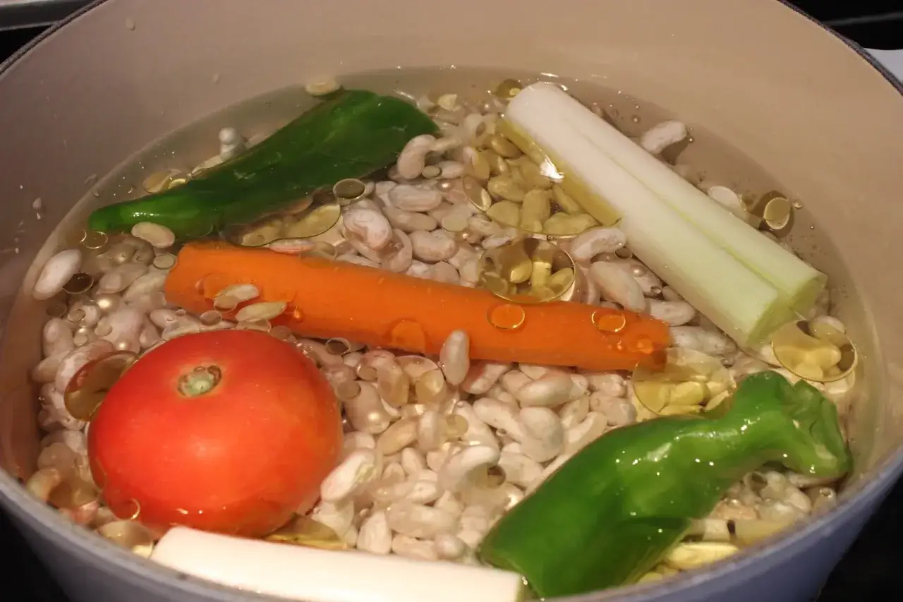 Pochas a la riojana en cocci&oacute;n: jud&iacute;as blancas, zanahoria, tomate, pimiento verde y puerro en una olla.