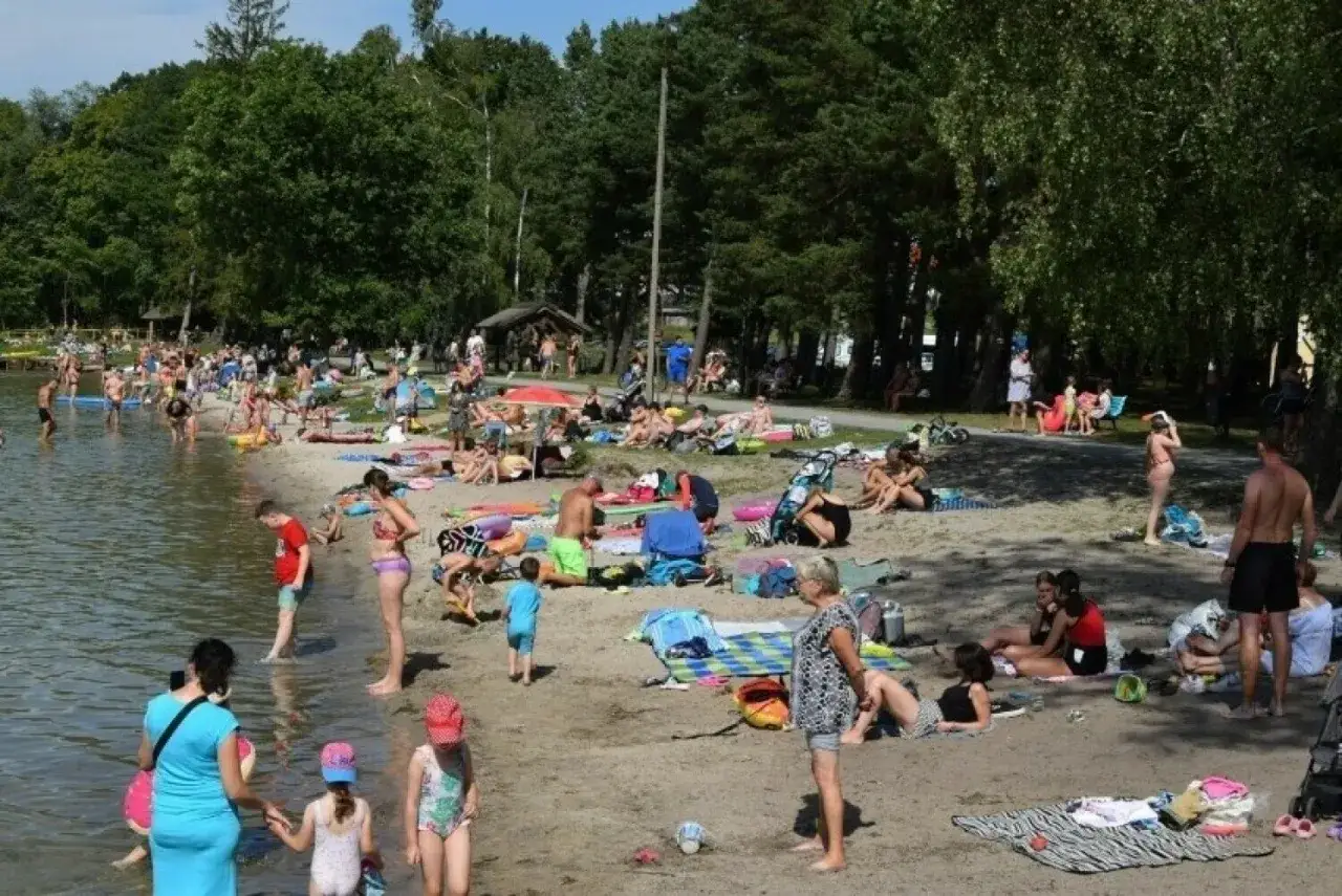 Tłum ludzi odpoczywa na piaszczystej plaży nad jeziorem w Wielkopolsce. Słońce, woda i relaks w letni dzień.