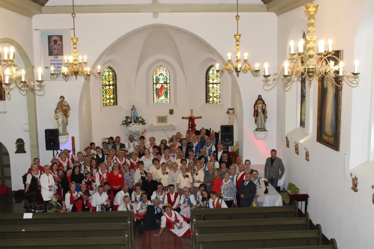 Grupa ludzi w strojach ludowych w kościele, przygotowująca się do przeglądu popularnych pieśni maryjnych.
