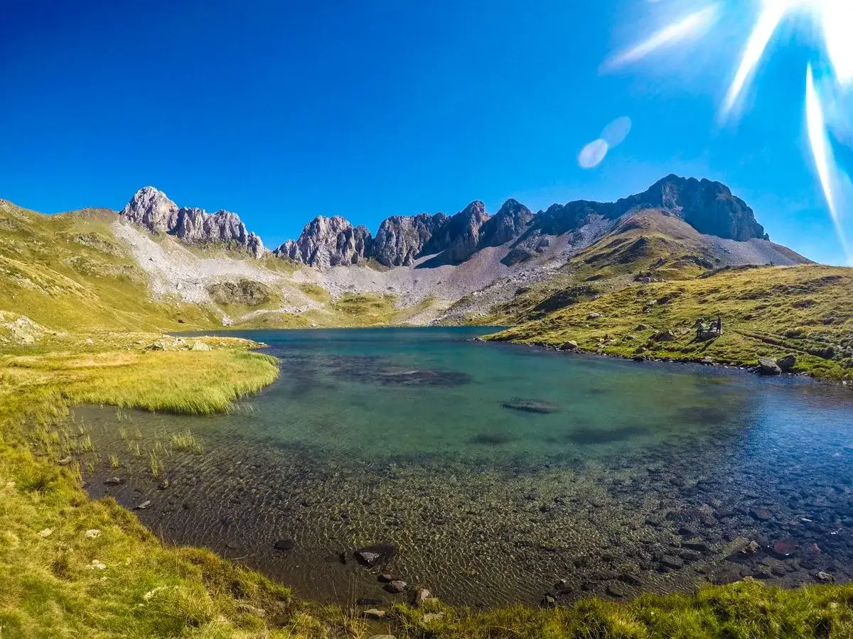 El ib&oacute;n de Acherito, un lago de monta&ntilde;a de aguas cristalinas, rodeado de prados verdes y picos rocosos bajo un cielo azul intenso.