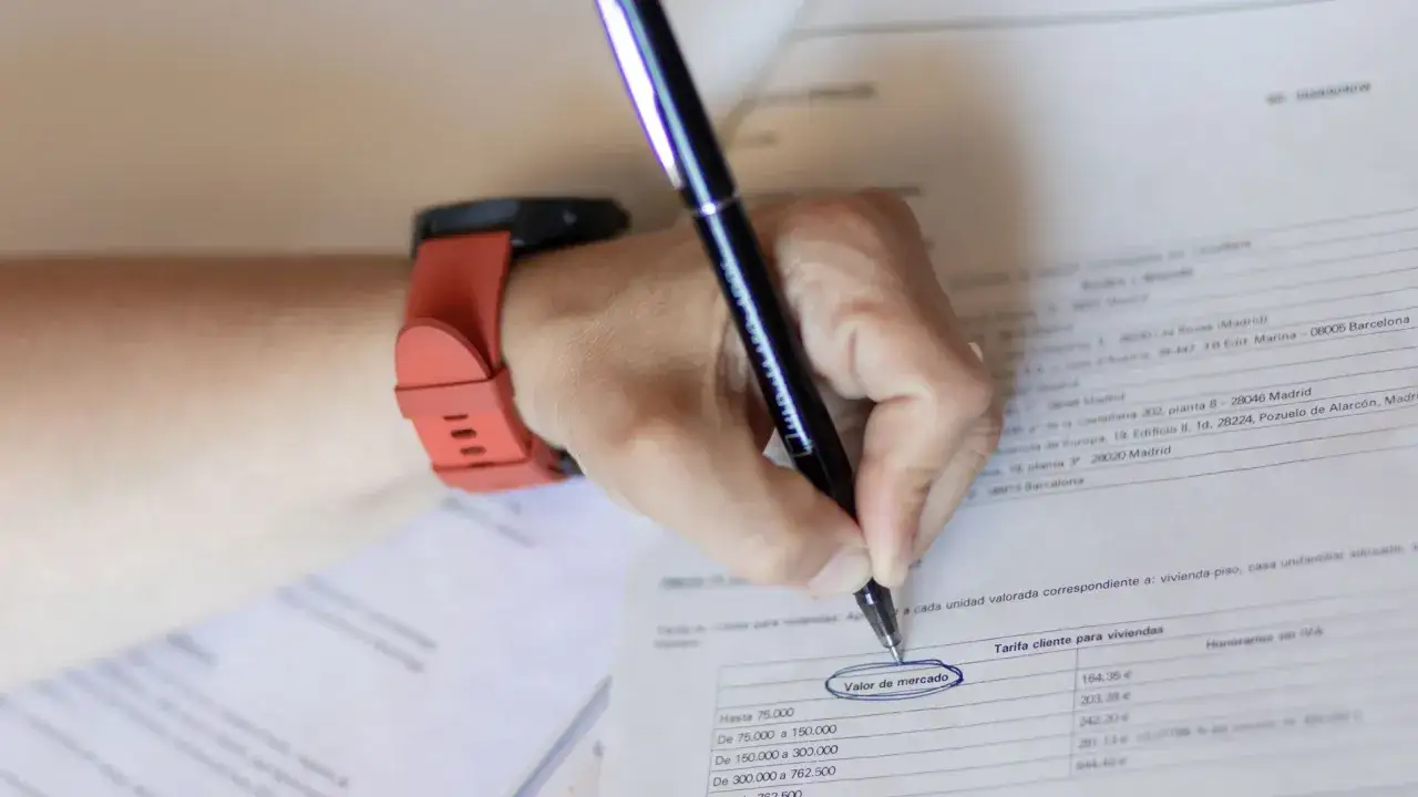 Mano con reloj rojo escribe en documento. Se lee 