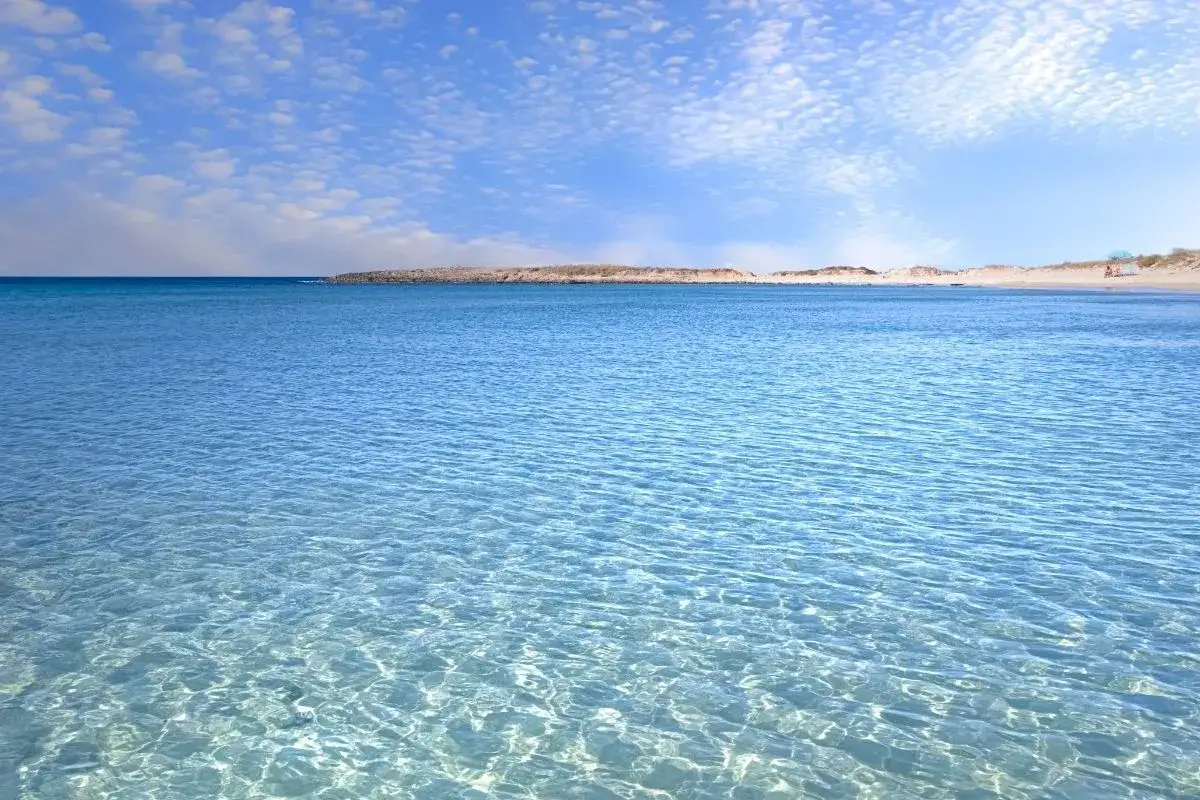 Acque cristalline e sabbia dorata a Lido Marini, Salento. Un paradiso azzurro sotto un cielo di nuvole bianche.