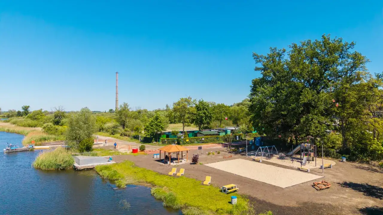 Nietypowe atrakcje Szczecin: plac zabaw, altana i pomost nad wodą. W tle komin i zieleń.