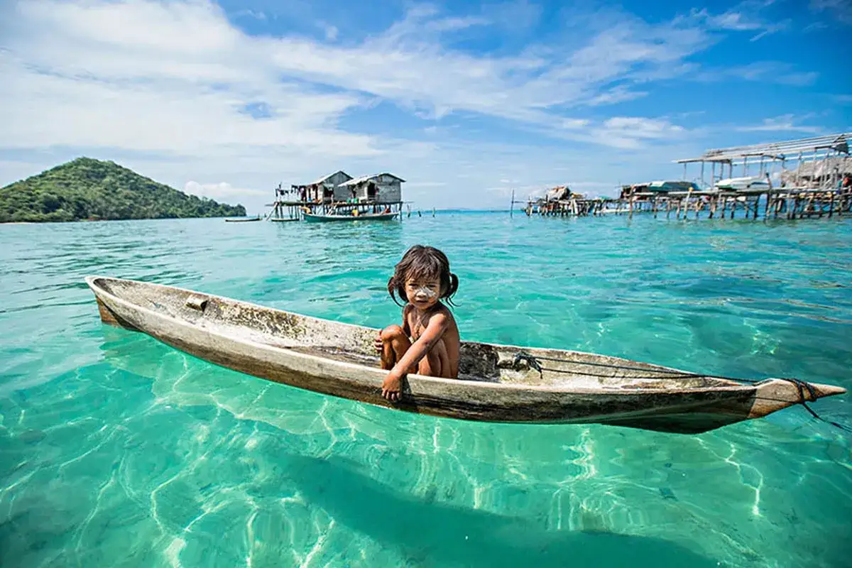 Bambina del popolo Bajau in una barca, circondata da acque turchesi e palafitte.
