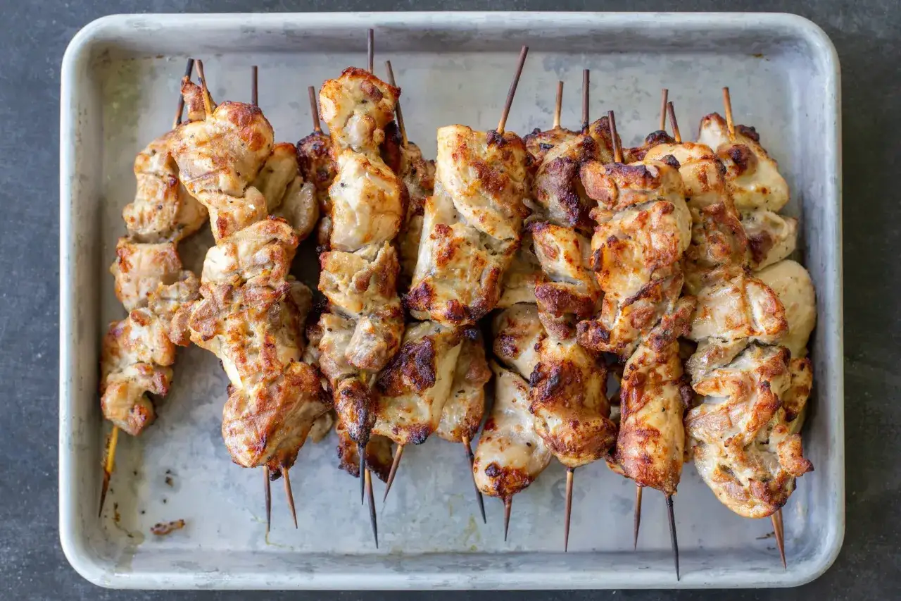 Domowy kebab z kurczaka z piekarnika na patyczkach, apetycznie przypieczony, leży na metalowej tacce.