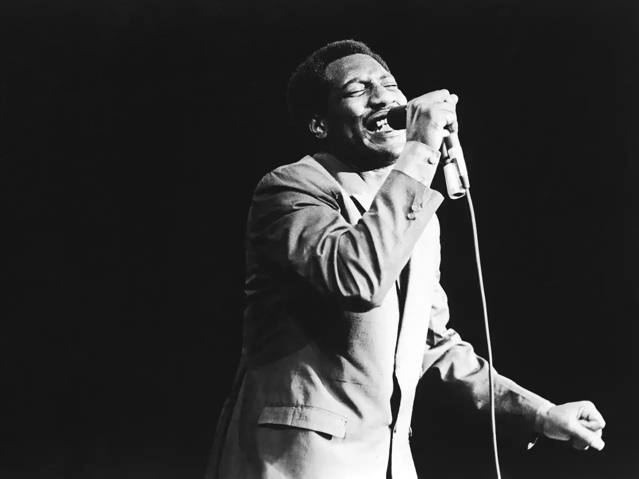Otis Redding singt mit geschlossenen Augen und voller Leidenschaft in die Mikrofongerät. Sein Titel von Otis Redding hallt durch den dunklen Raum.
