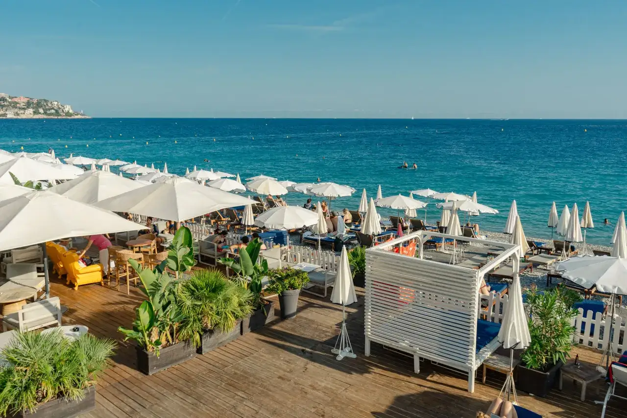 Entspannter nizza strand mit vielen wei&szlig;en Sonnenschirmen, Liegest&uuml;hlen und dem blauen Meer im Hintergrund.