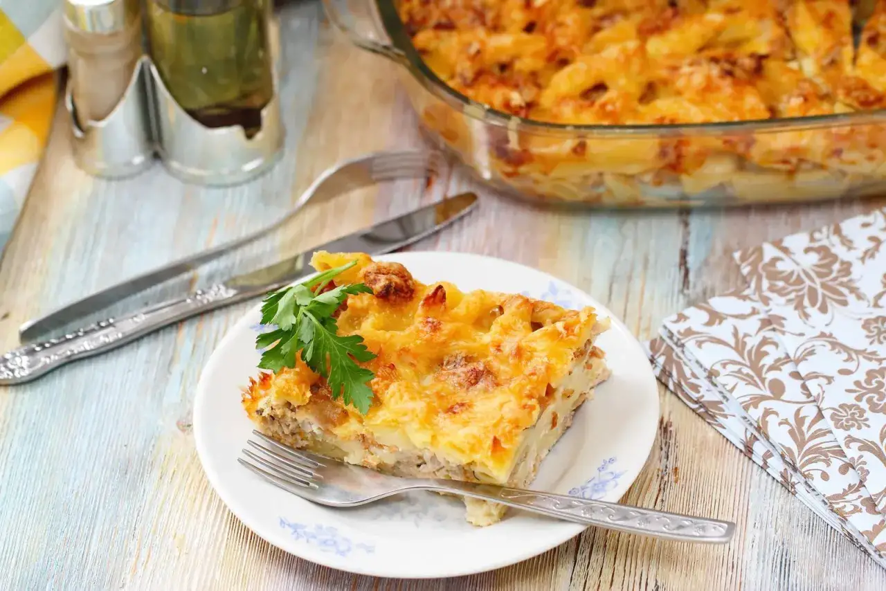 Una fetta di pasta al forno bianca napoletana, dorata e filante, guarnita con prezzemolo fresco. Sullo sfondo, la teglia piena.