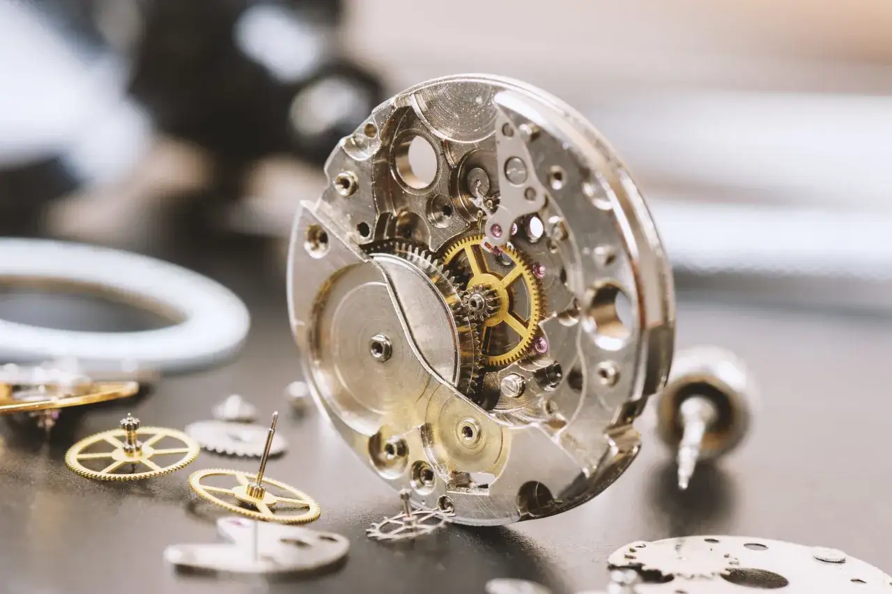 Precyzyjny mechanizm zegarka, z widocznymi kołami zębatymi i sprężynami, czeka na złożenie. To serce czasomierza, jego mechanizm.