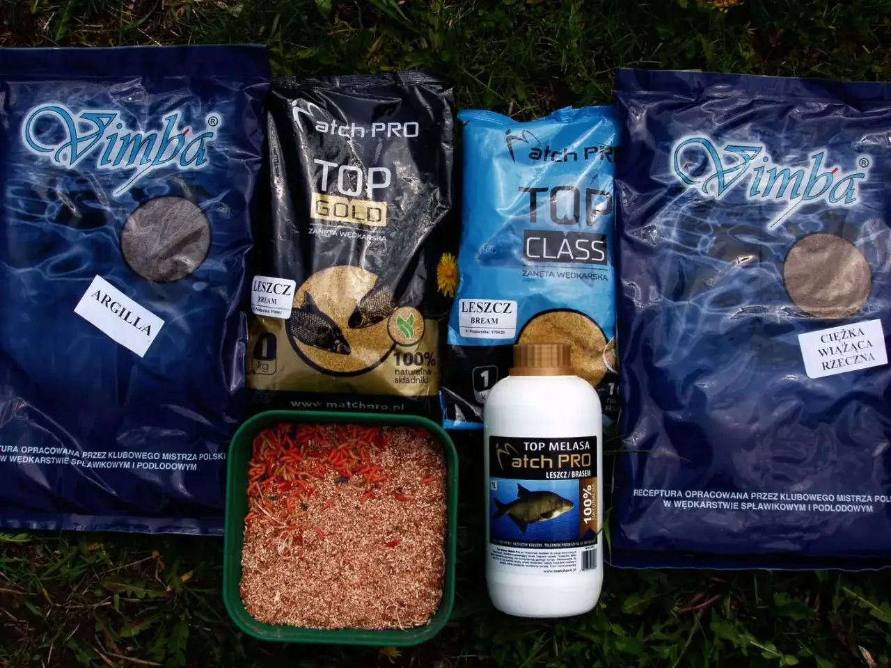 Zanęty Match PRO: Top Gold, Top Class, Vimba Argilla i Vimba Ciężka Wiążąca Rzeczna, a także melasa. Obok pojemnik z ochotką i robakami.
