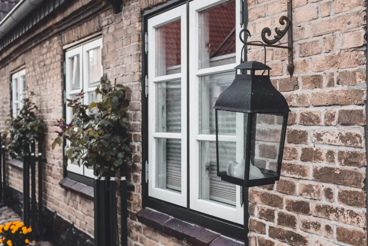 En gammal tegelfasad med vita fönster och en svart lykta. Kanske dags att måla tegelfasad för att ge den nytt liv?