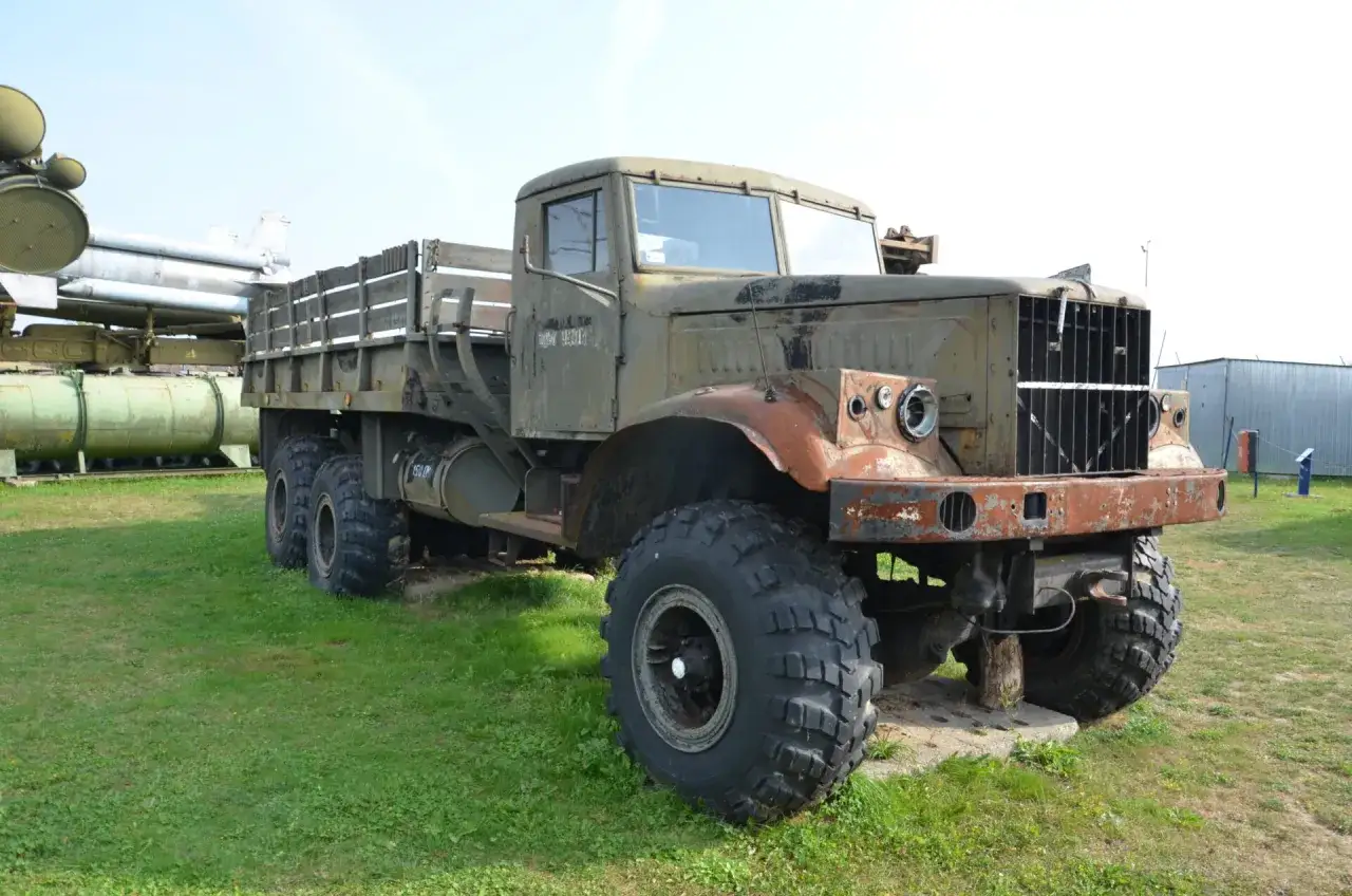 Kraz 255, stary, zardzewiały, wojskowy samochód ciężarowy z drewnianą skrzynią ładunkową, stoi na trawie obok rakiet.