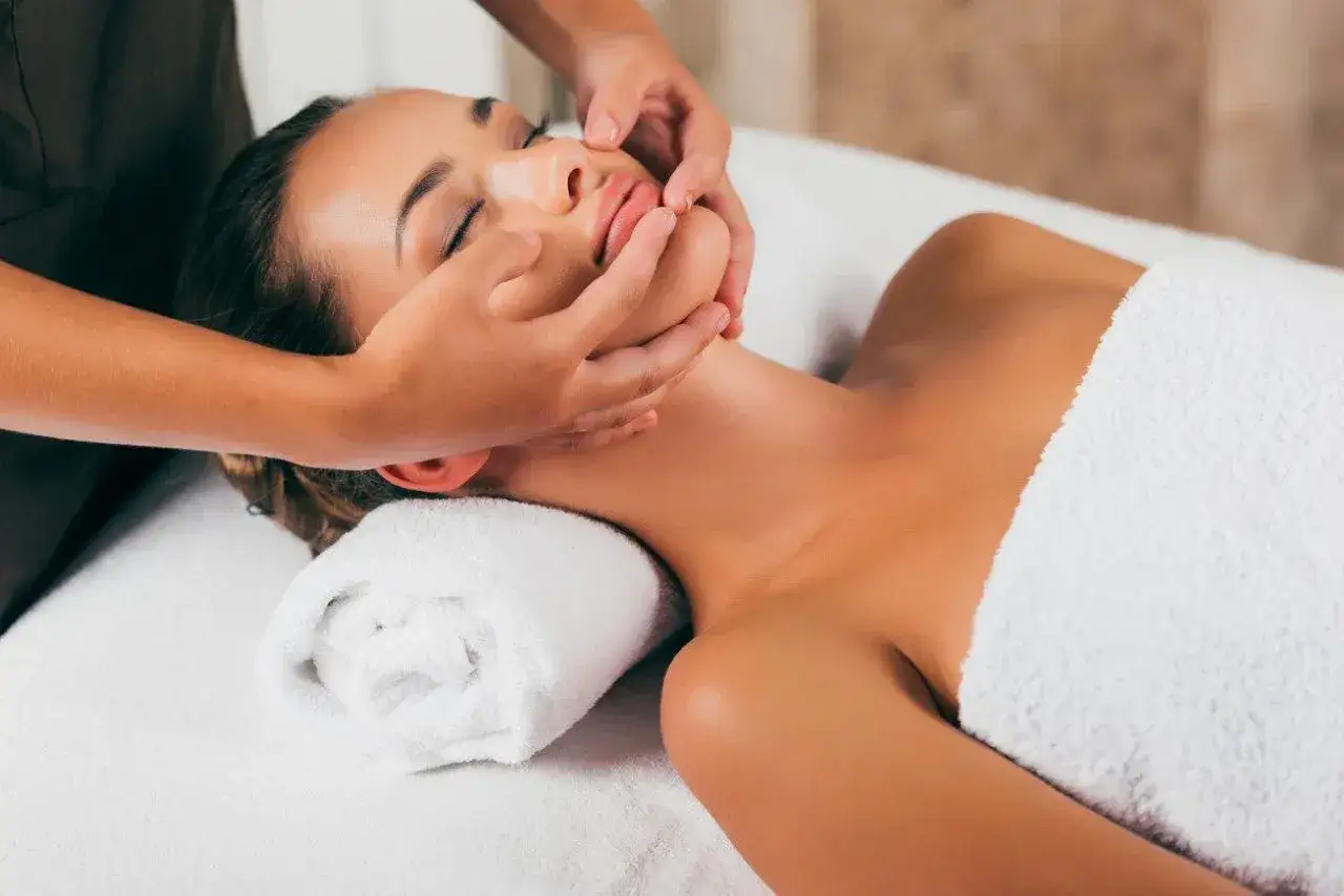 A woman enjoys a relaxing facial massage, her eyes closed in bliss. The gentle touch of the therapist's hands soothes her skin.