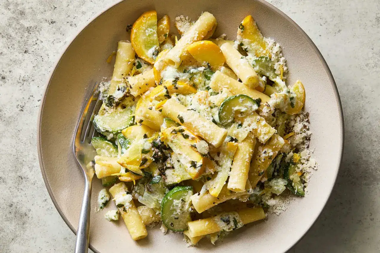 En tallrik med rigatoni pasta blandad med skivad zucchini och gul squash, toppad med riven ost och &ouml;rter. En h&auml;rlig zucchini pasta-r&auml;tt.