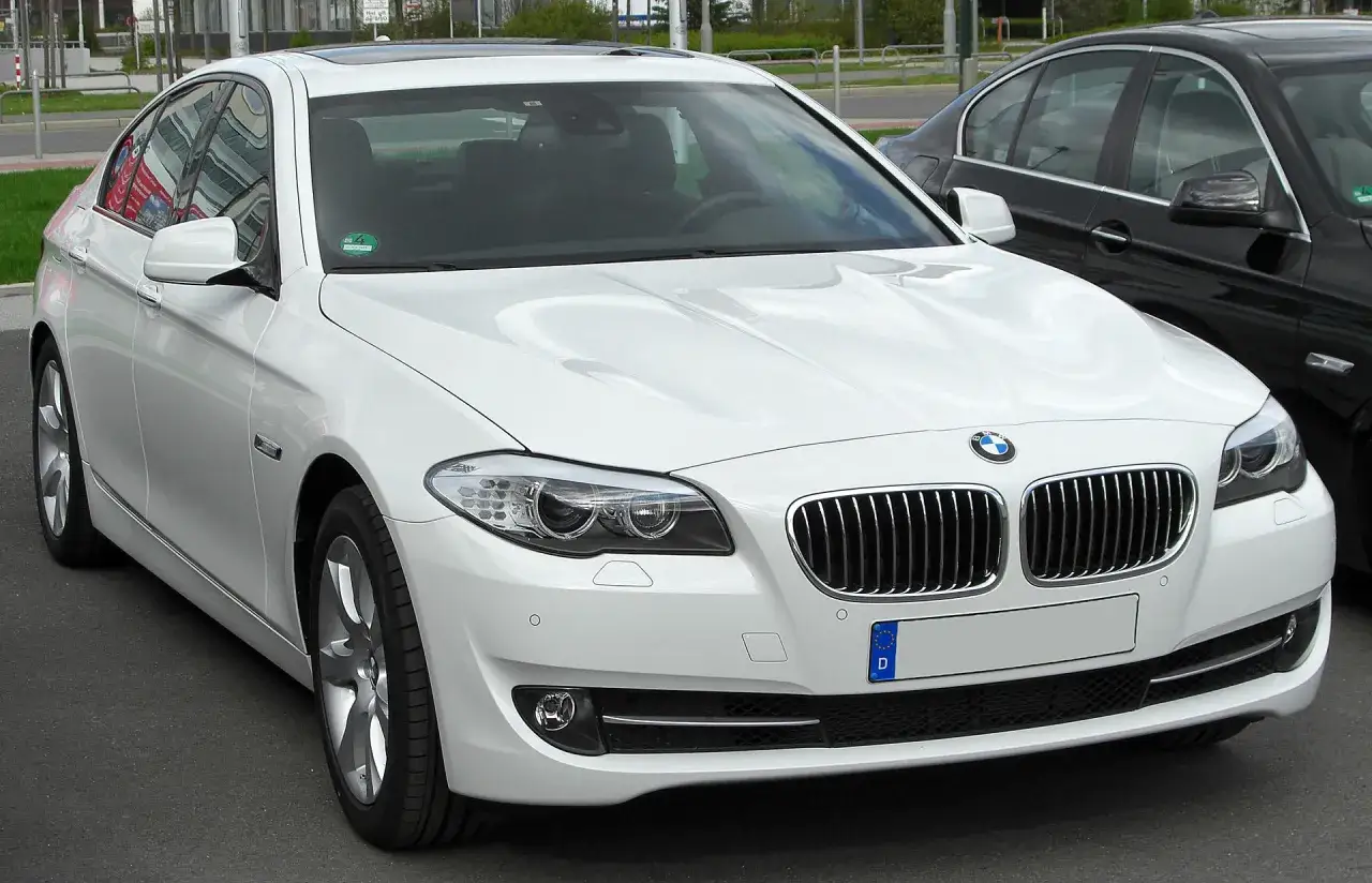 Białe BMW 535d z charakterystycznym grillem i reflektorami, zaparkowane obok czarnego samochodu.