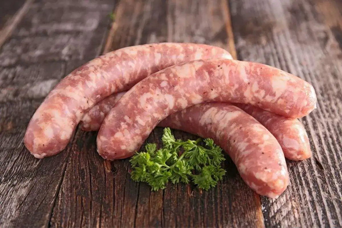 Surowe kiełbaski na drewnianym blacie, ozdobione gałązką natki. Zastanawiasz się, ile m mają jelita?
