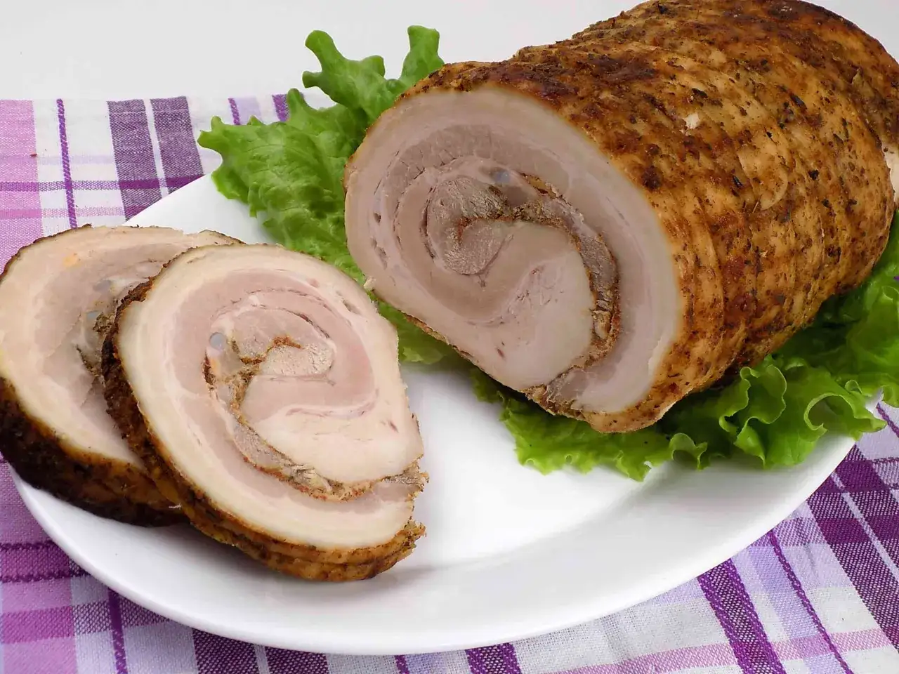 Pyszna rolada z boczku, pokrojona w plastry, podana na liściach sałaty.