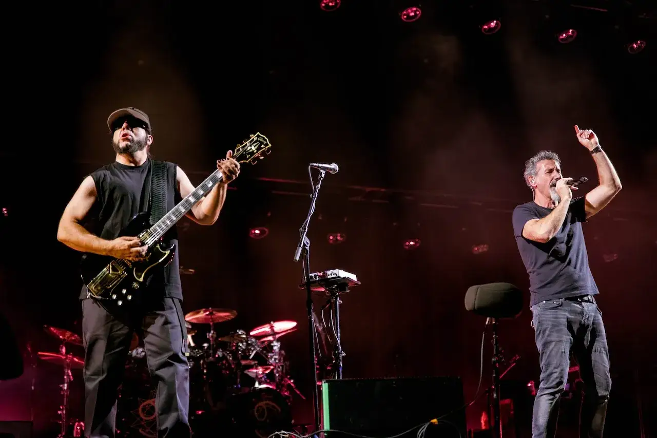 Les membres de System of a Down en pleine performance, un guitariste à gauche, le chanteur à droite, sous des lumières tamisées.