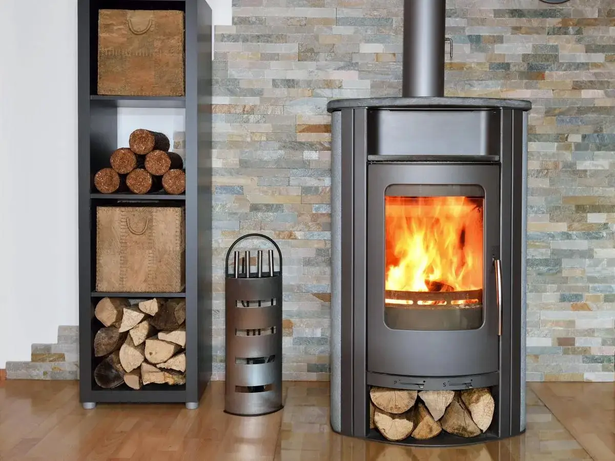 Ein Kaminofen mit brennendem Feuer, daneben ein Regal mit Holz und Körben. Ausnahmen für das Stilllegen von Kaminöfen sind selten.