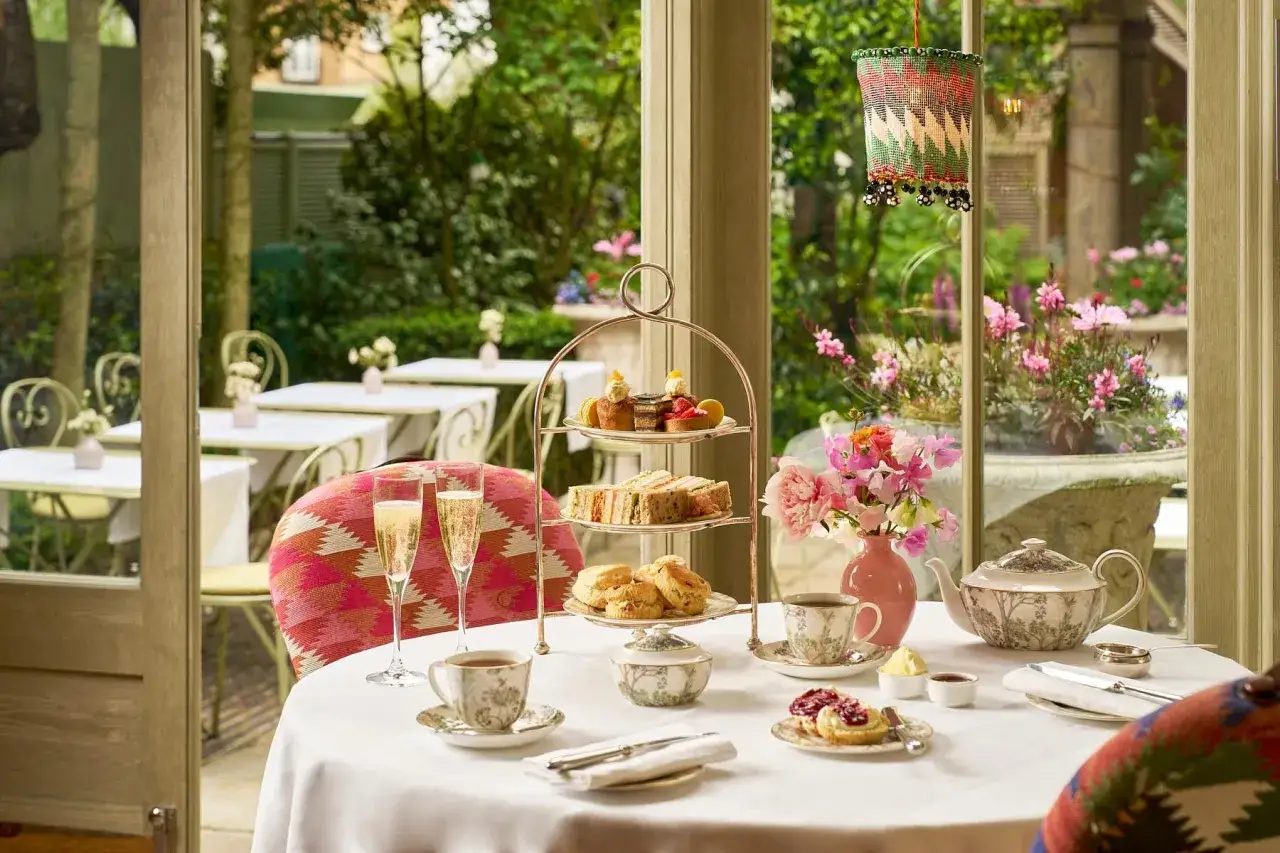 Un elegante afternoon tea a Londra: dolci, tramezzini, scones e champagne, con un giardino fiorito sullo sfondo.