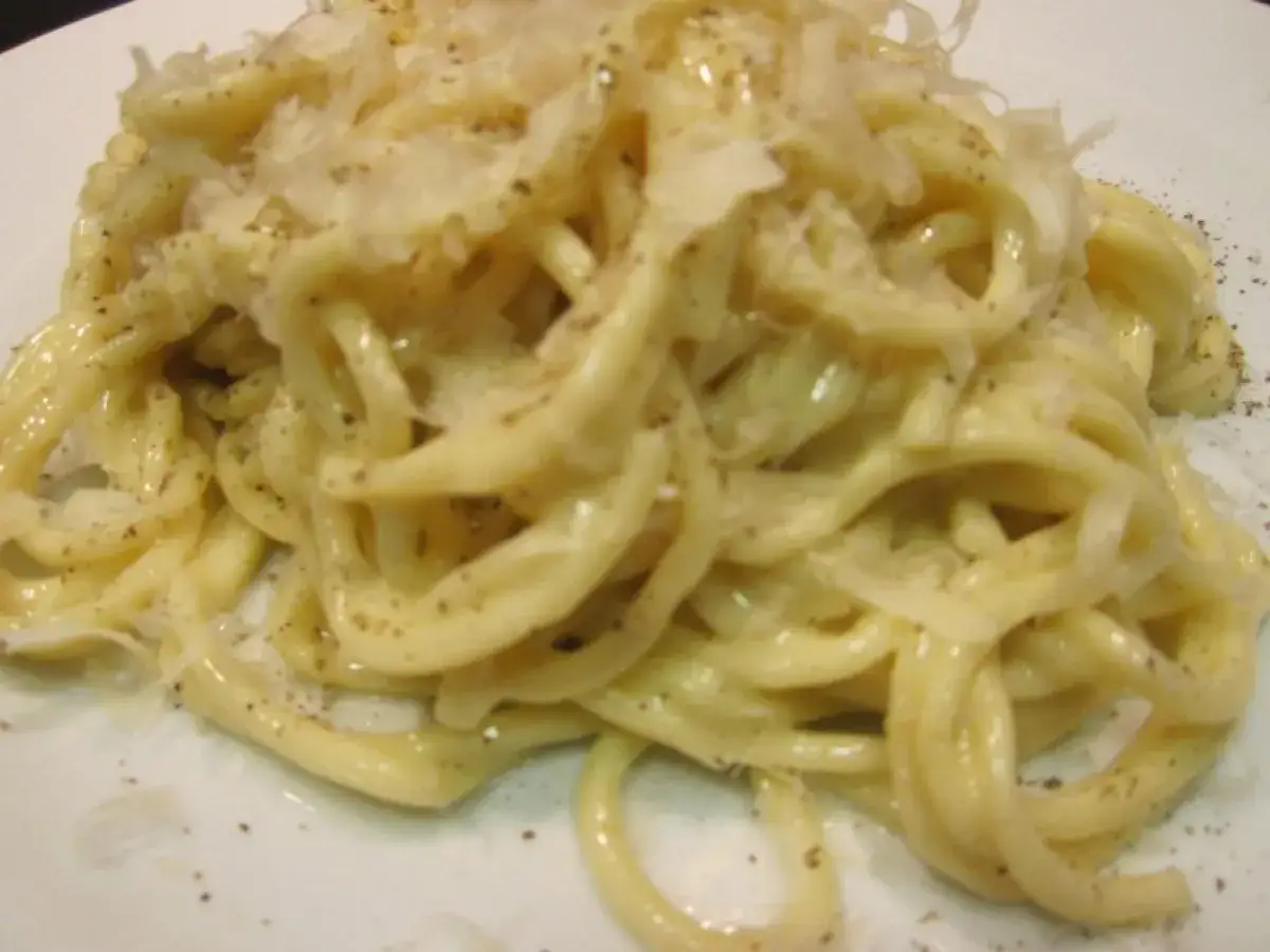 Un plato de cacio e pepe, pasta cremosa con queso pecorino y pimienta negra, espolvoreado con más queso rallado.