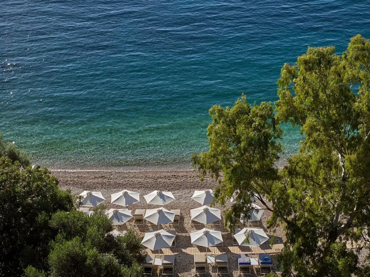 Alkyna Lifestyle Beach Resort: Sonnenschirme und Liegen am Kiesstrand, türkisfarbenes Meer.