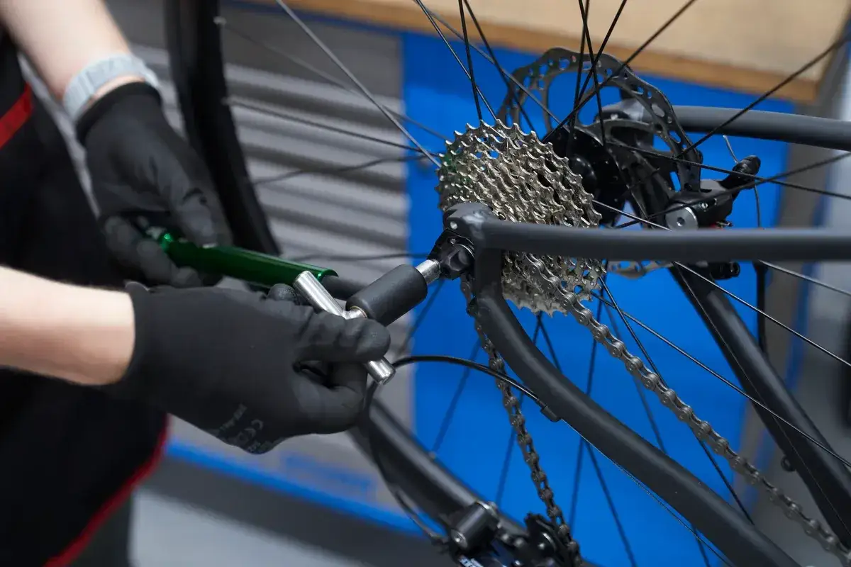 Mechanic uses a tool to straighten a bent derailleur hanger on a bicycle's rear cassette.