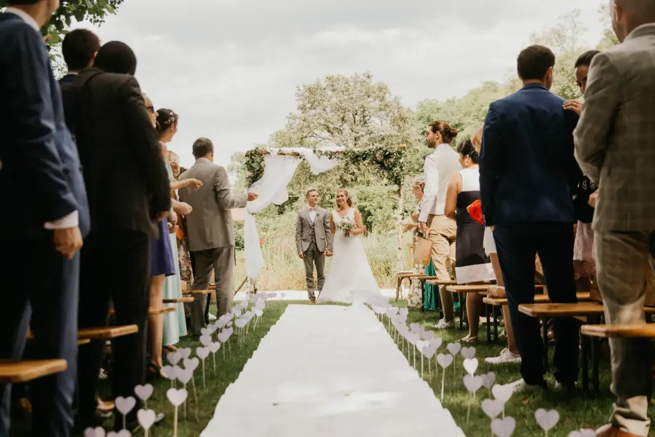 Un couple de mari&eacute;s marche sur un tapis blanc, entour&eacute; d'invit&eacute;s, lors d'une c&eacute;r&eacute;monie la&iuml;que exemple.