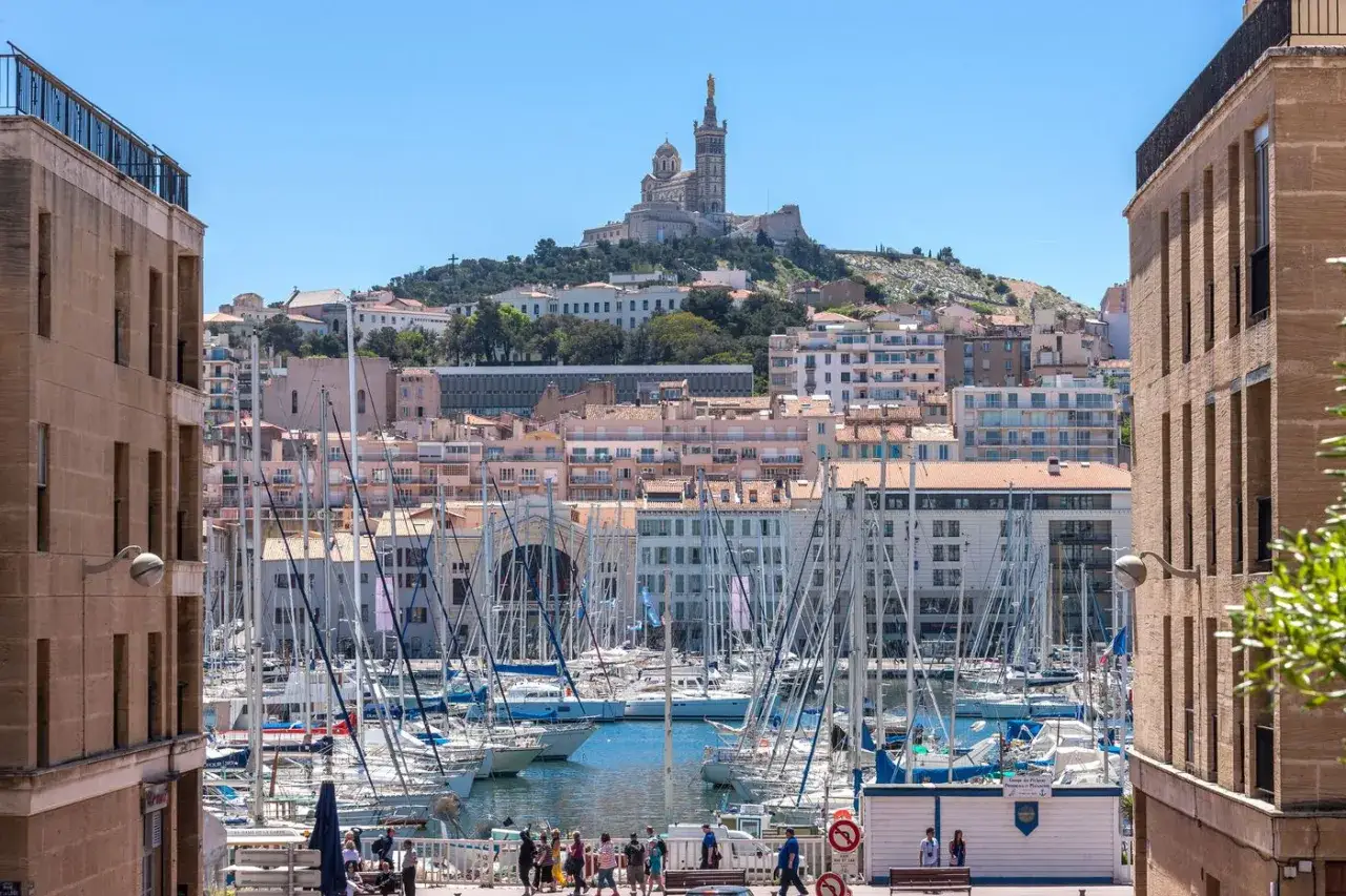 Widok na port w Marsylii z licznymi żaglówkami i bazyliką Notre-Dame de la Garde na wzgórzu.