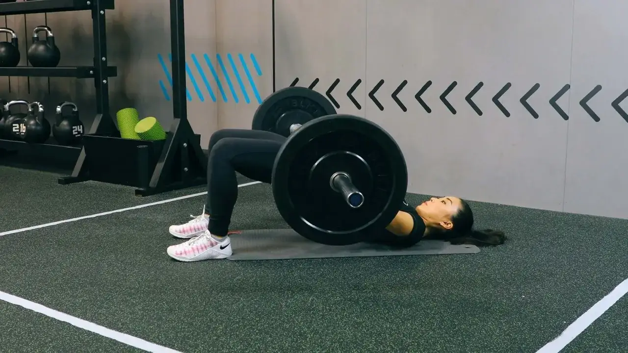 Frau macht Glute Bridge mit Langhantel.