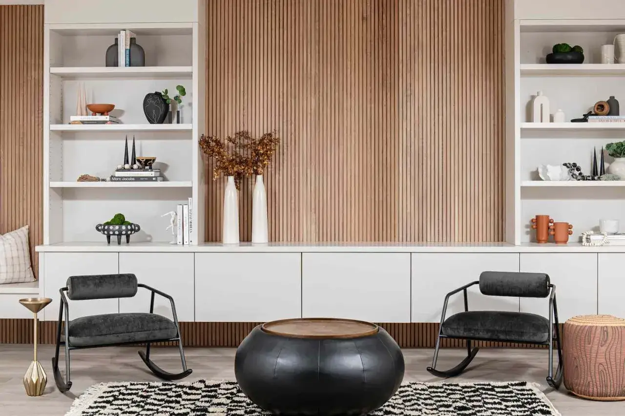 Moderne wohnzimmer wandgestaltung mit Holzlamellen und wei&szlig;en Regalen, zwei dunklen Schaukelst&uuml;hlen und einem runden Couchtisch.