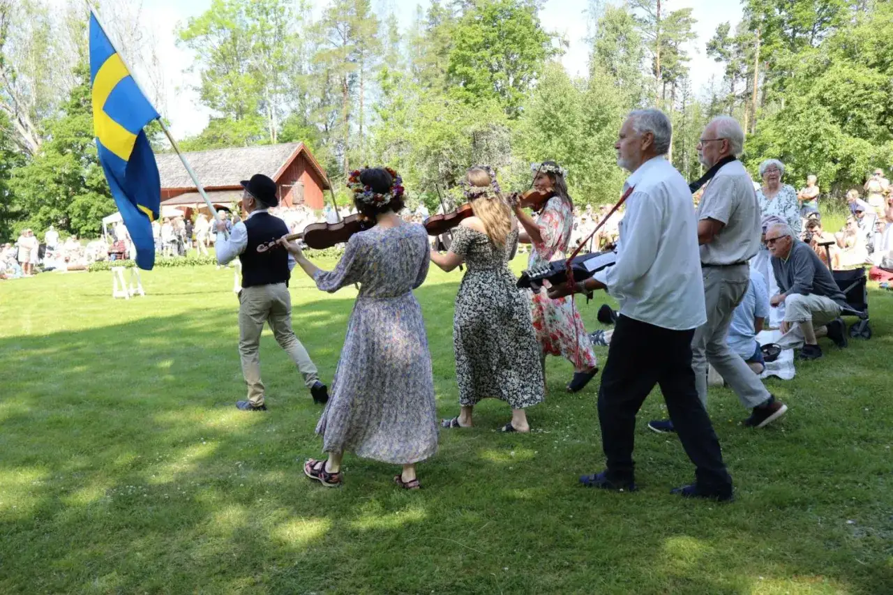 Musikerna spelar på midsommarafton. En svensk flagga vajar i bakgrunden.