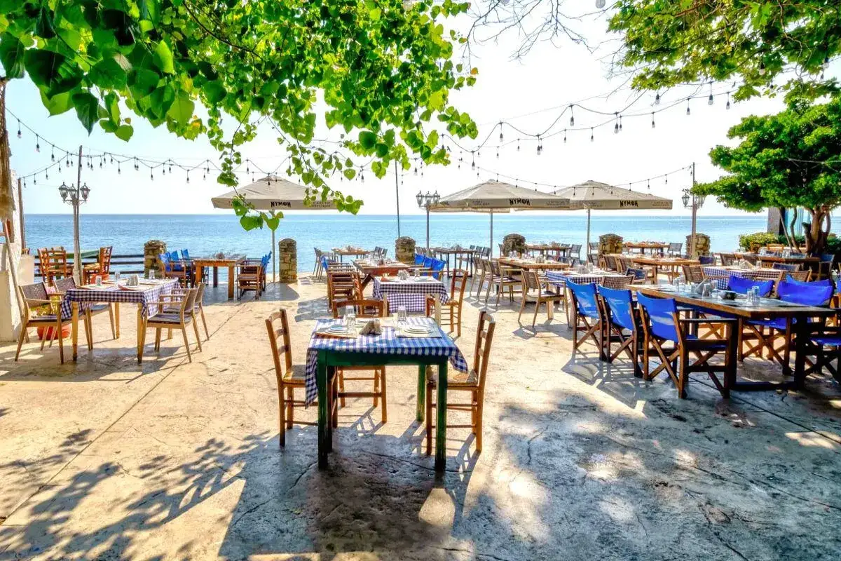 Taras restauracji nad morzem, stoliki z niebiesko-białymi obrusami. Idealne miejsce na wakacje all inclusive – co to znaczy? Pełen relaks!