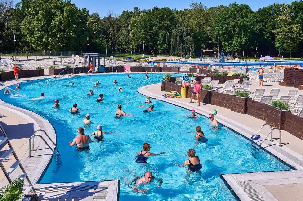 Grupa osób ćwiczy w basenie, szukając fajnych miejsc nad wodą łódzkie. Słońce, woda i aktywność fizyczna to idealne połączenie.