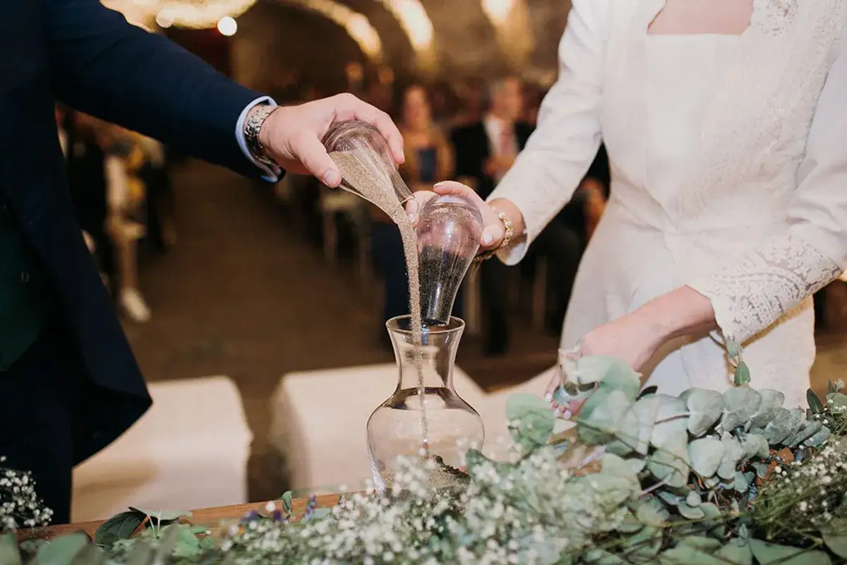 Manos de novios vierten arena en un jarr&oacute;n, simbolizando el ritual de la arena boda. Sus vidas se unen, como la arena que se mezcla.