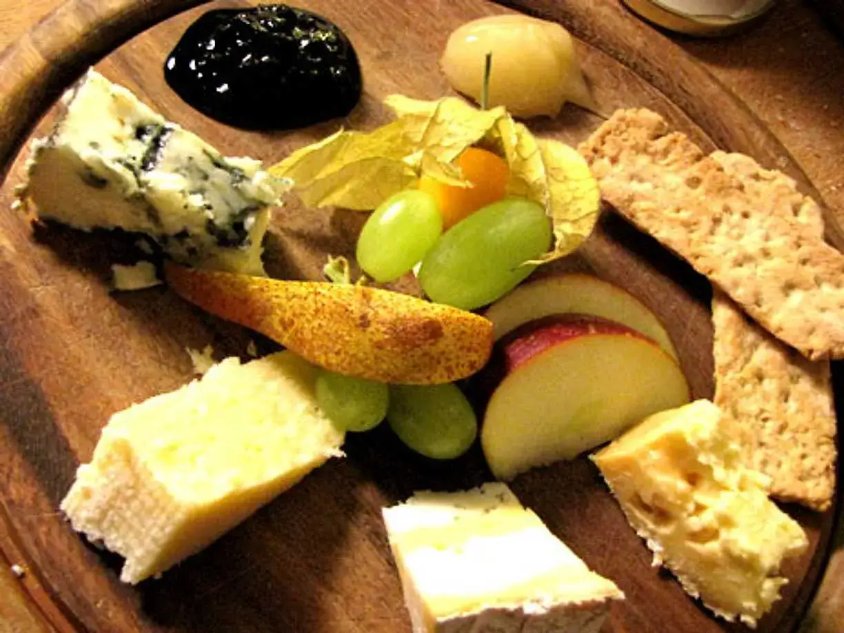 Ostbricka med olika ostar, vindruvor, äpple, päron och en klick mörk marmelad till ost.