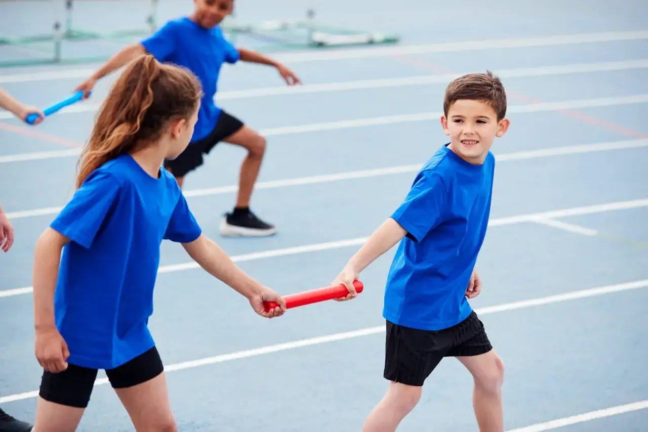 Ni&ntilde;os en una pista de atletismo, pasando un testigo. &iexcl;Perfecto para juegos para jugar con amigos sin material!