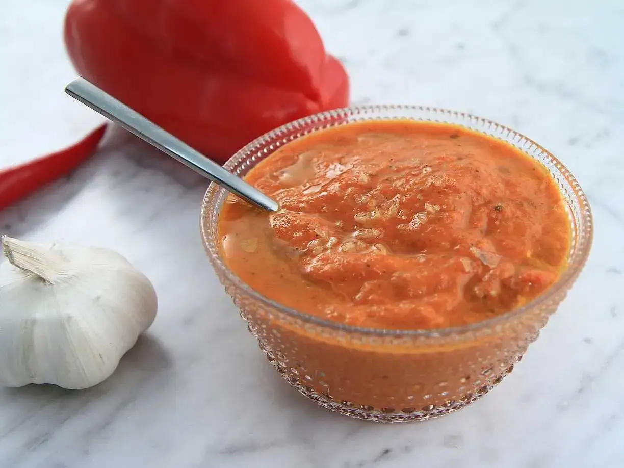 En skål med en härlig aivar, med en röd paprika, chili och vitlök i bakgrunden.