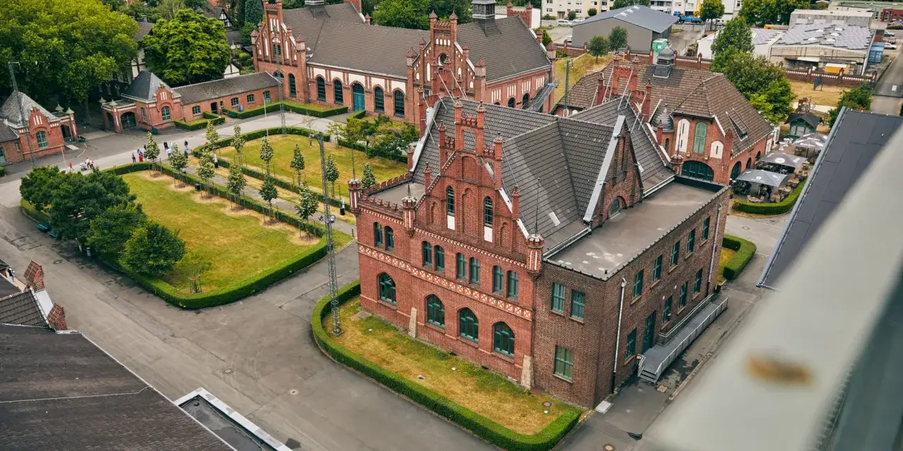 Historische Backsteingebäude des Zollern-Kraftwerks mit begrünten Innenhöfen und Bäumen.