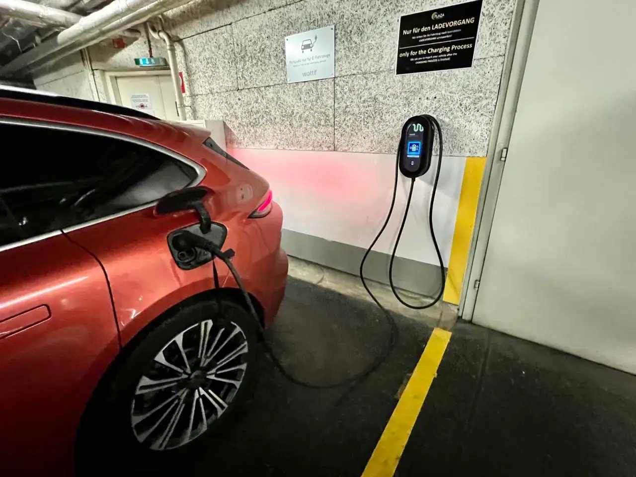Pomarańczowy samochód elektryczny ładuje się w garażu. Od września 2026 r. każdy blok musi mieć punkt ładowania aut elektrycznych, co ułatwia przyszłość.