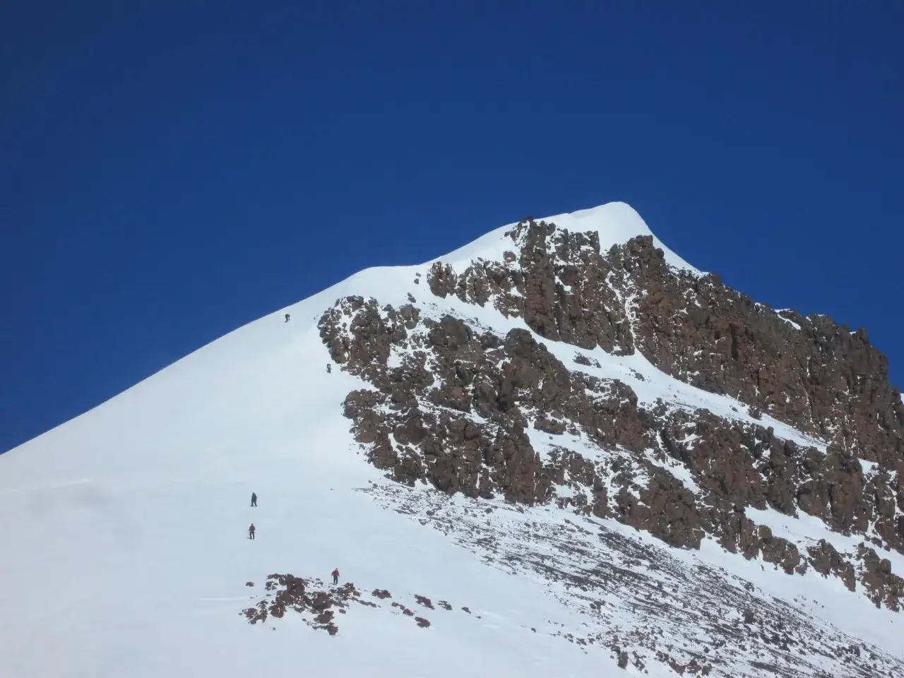 Grupa alpinist&oacute;w wspina się na najwyższy szczyt Grenlandii. Skaliste zbocza pokryte śniegiem i lodem.