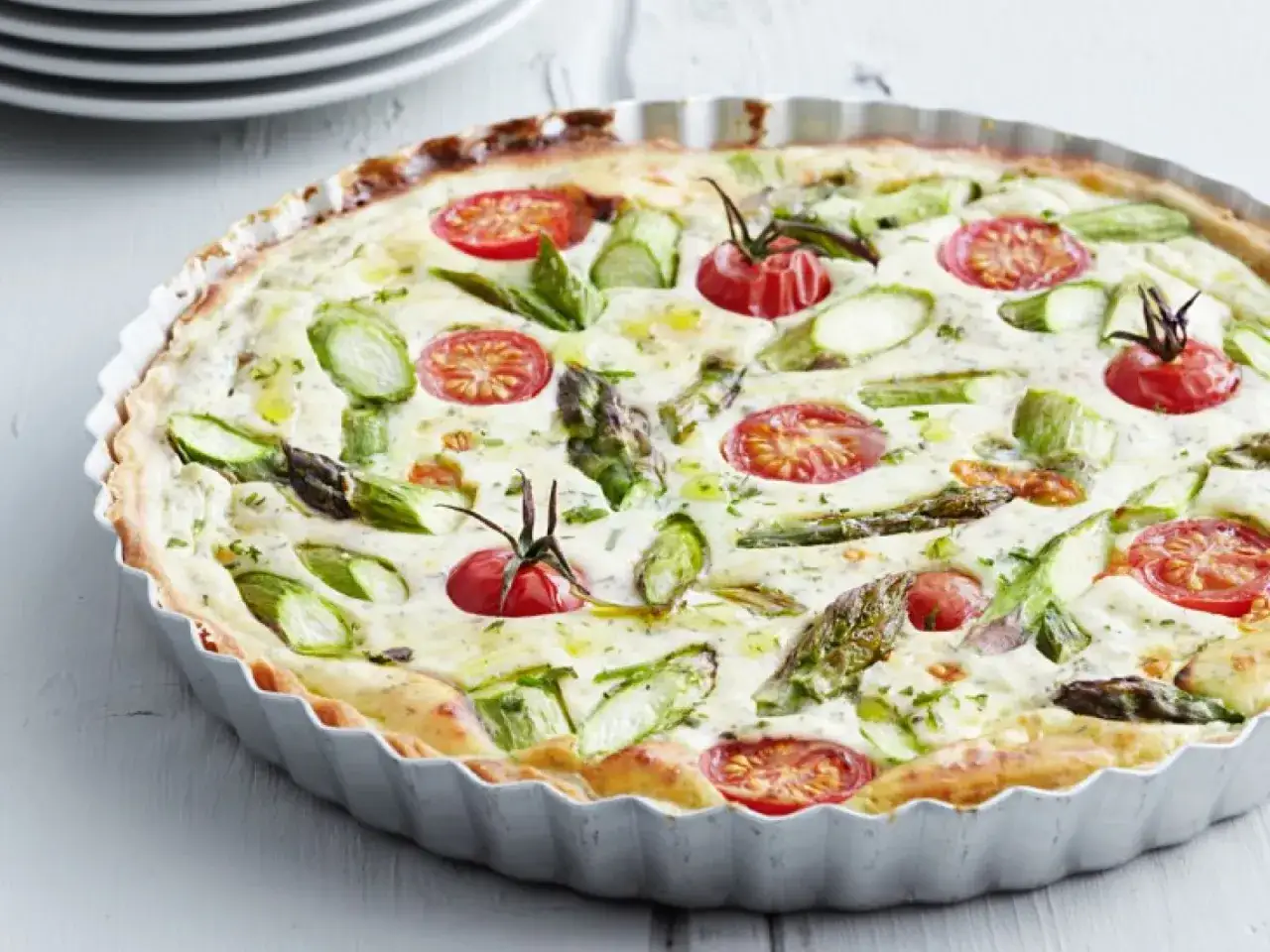 Frische sommer quiche mit Spargel und Kirschtomaten in einer Metallform, bereit zum Servieren.