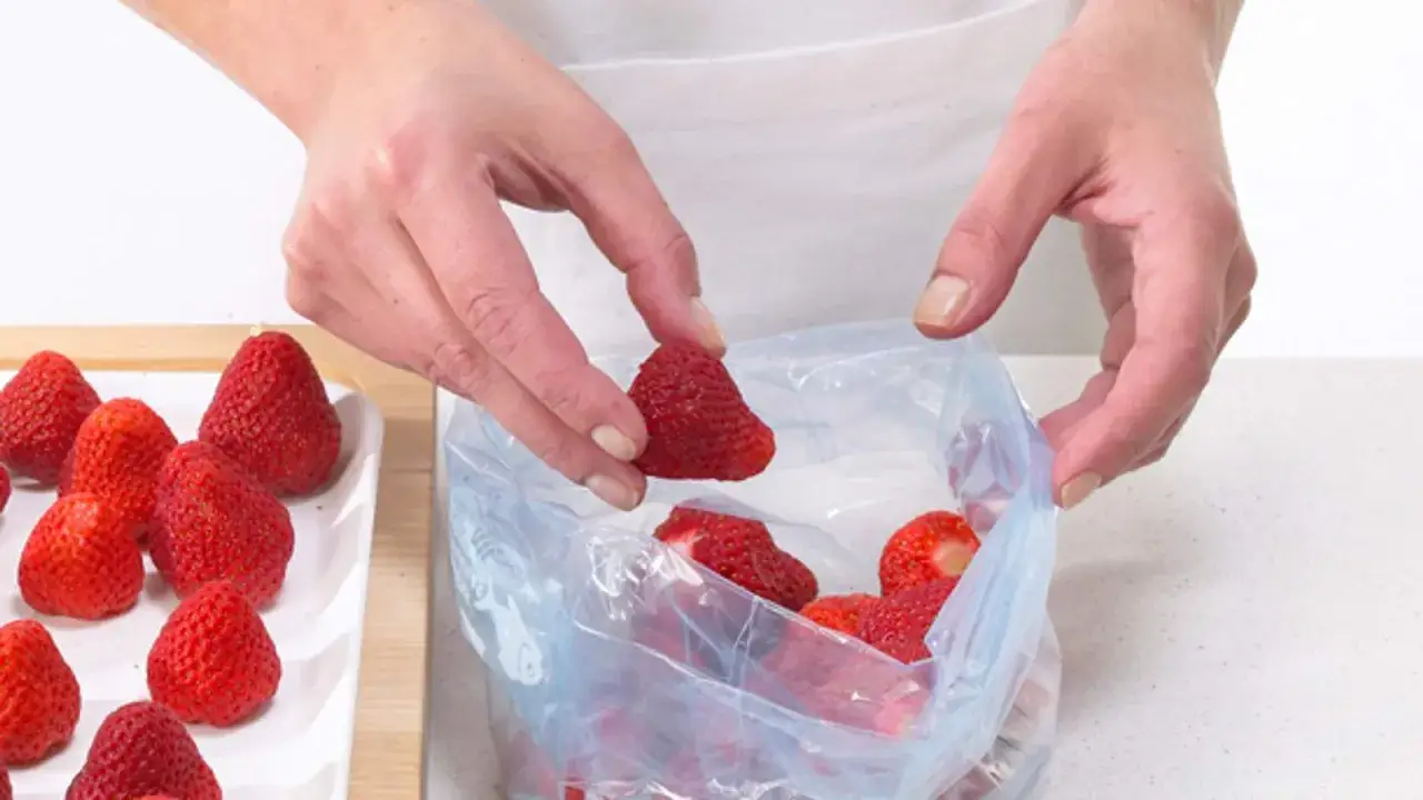 Hände legen frische Erdbeeren in einen Gefrierbeutel. So einfach ist das Erdbeeren einfrieren für später.