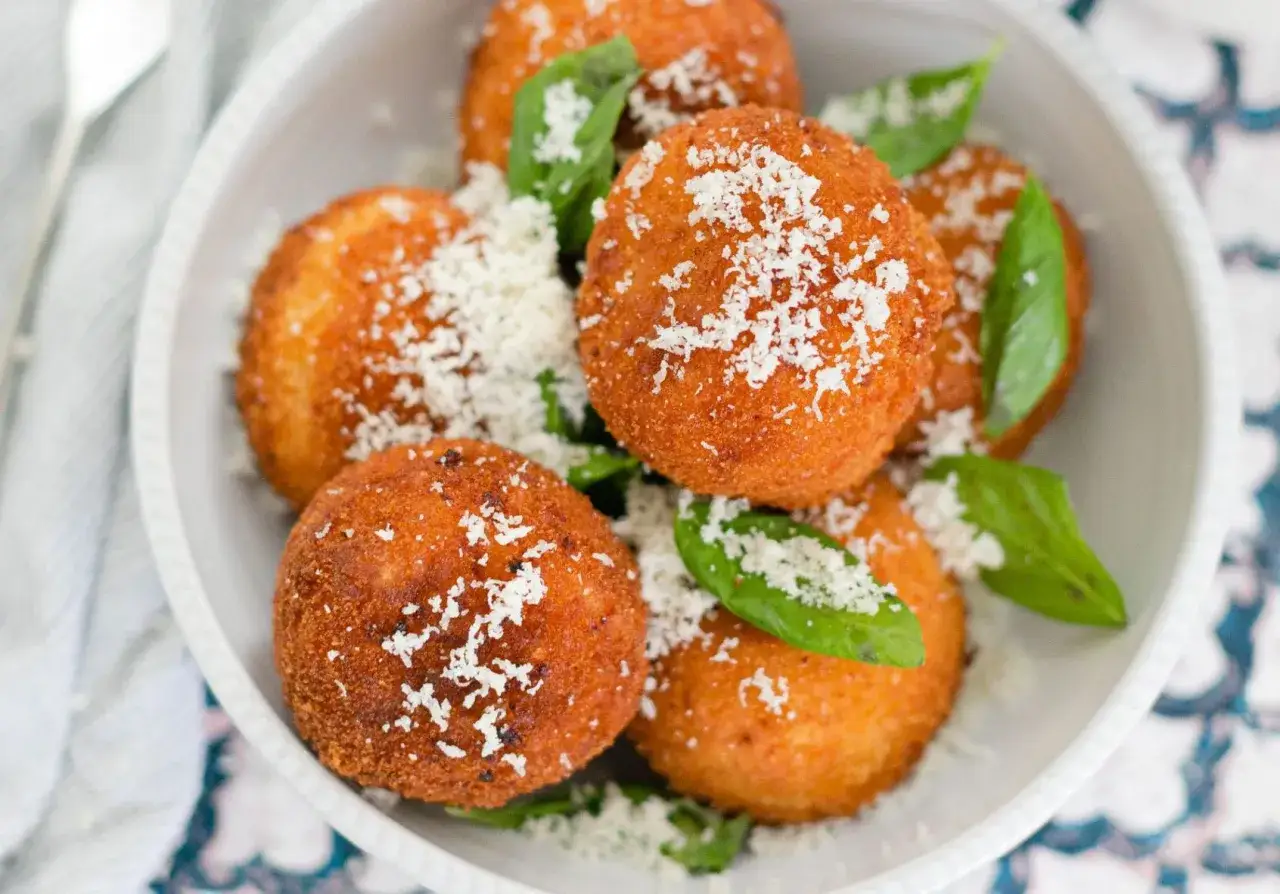 Un plat de sp&eacute;cialit&eacute; italienne arancini, ces boules de riz pan&eacute;es et frites, garnies de parmesan r&acirc;p&eacute; et de feuilles de basilic frais.